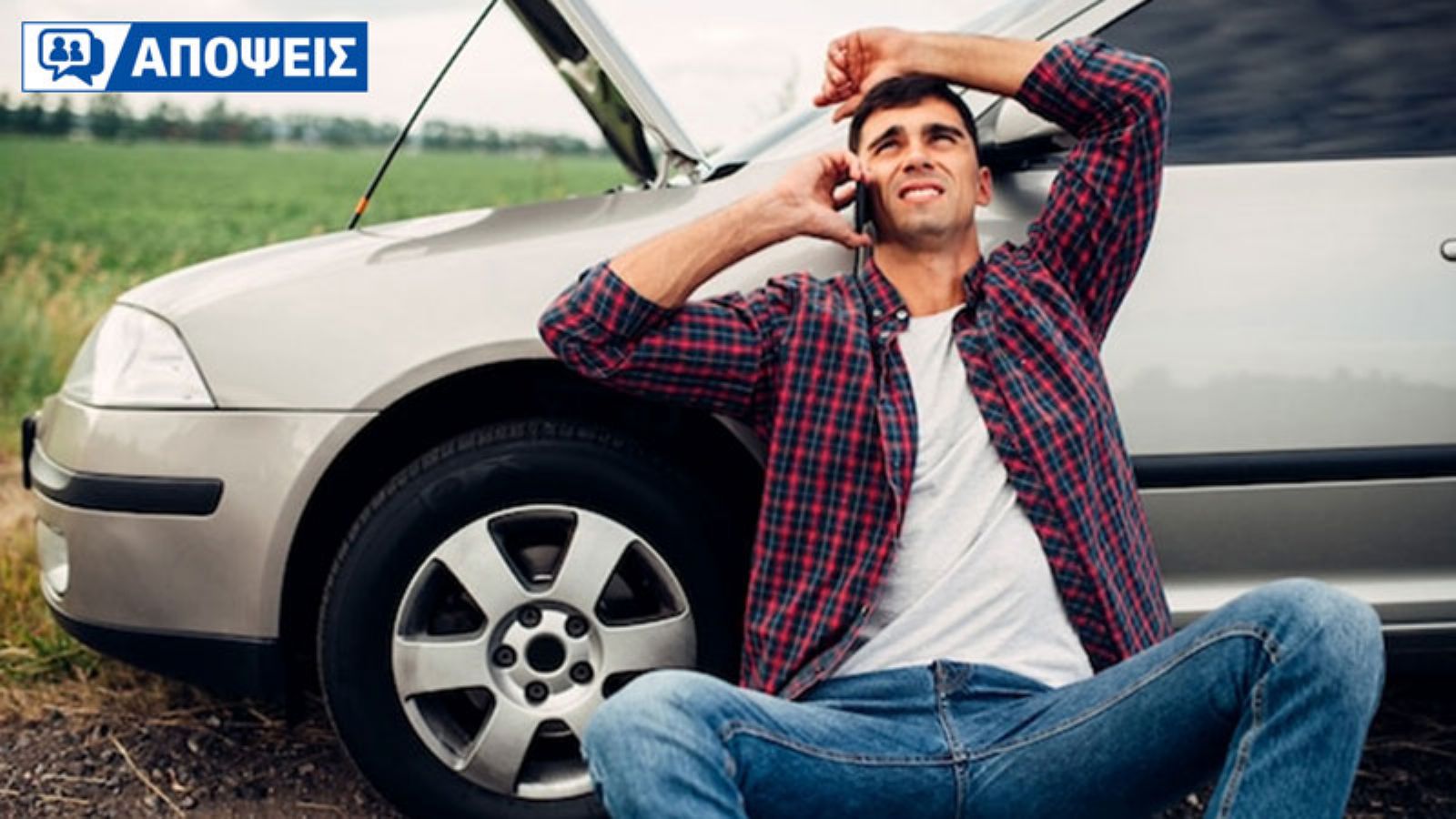 ¶νθρωπος που κάθεται δίπλα από το αυτοκίνητό του με ανοιχτό το καπό, μιλώντας στο κινητό επειδή έχει πάθει βλάβη.